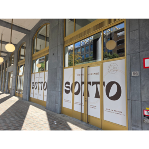 De gevel met de beplakte ramen onder een galerij, waar het ontwerp over meerdere panelen doorloopt.